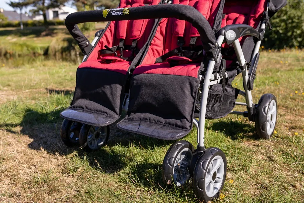 Assistante maternelle promenant des enfants dans une poussette multiple sur un trottoir français